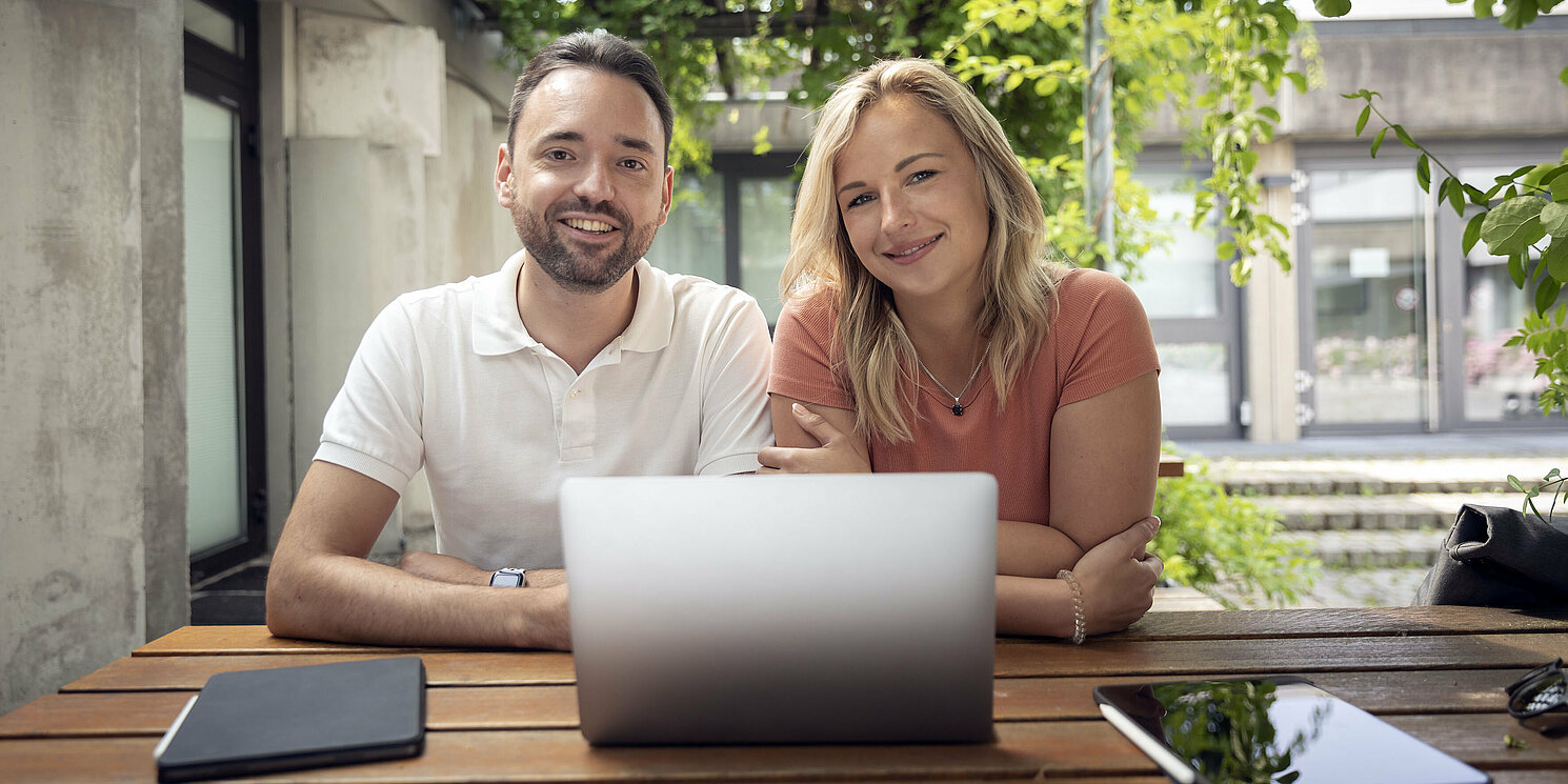A man and a woman sit in front of a laptop in a courtyard